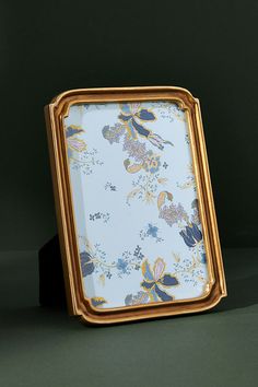 a gold frame with a blue and yellow floral pattern on the front, sitting on a green surface