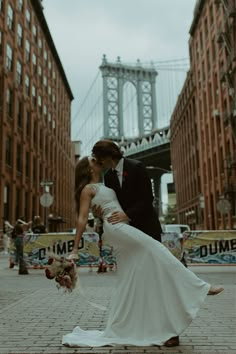 a bride and groom are kissing in front of the brooklyn bridge on their wedding day