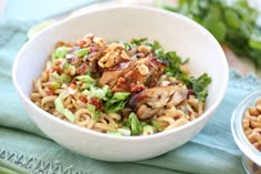 a white bowl filled with noodles and meat on top of a blue towel next to another bowl