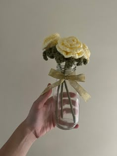 a hand holding a glass jar with flowers in it and a ribbon around the top