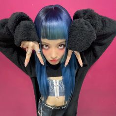 a young woman with blue hair and black gloves on her head, posing in front of a pink background