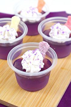 four desserts in plastic cups on a cutting board with purple and white frosting