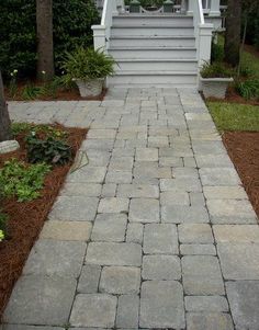 a white house with steps leading up to the front door and side porch area that is made out of pavers