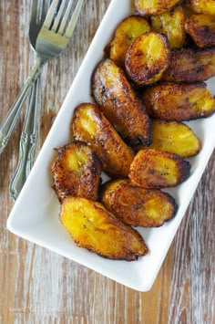 grilled bananas in a white dish with a fork and knife next to it on a wooden table