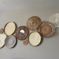 several woven baskets hanging on the wall with a mirror in front of them and another piece of artwork behind it