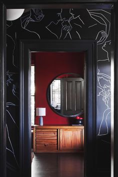 an entry way with red walls and black painted wall paper on the door, along with a round mirror