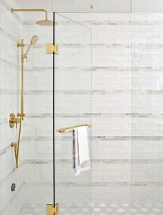 a white tiled bathroom with gold fixtures and glass shower door, along with two towels hanging on the wall