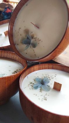 three wooden bowls filled with white liquid and some dried flowers in the inside one bowl