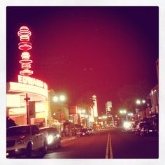 cars are parked on the side of the road in front of a movie theater at night