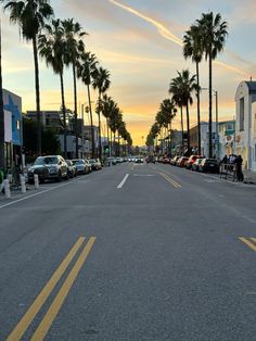 a street lined with palm trees and parked cars on both sides at sunset or dawn