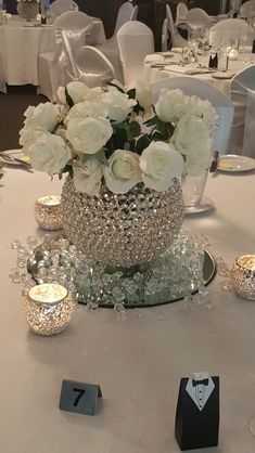 the centerpieces on this table are adorned with crystal beads and white roses, which were accented with candles