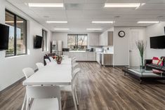 a large open living room and dining area with wood flooring, white walls and ceiling