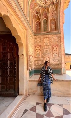 a woman standing in front of a building with intricately painted walls and doorways