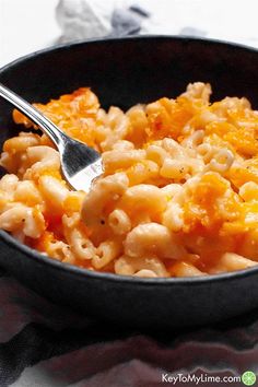 a bowl filled with macaroni and cheese on top of a table next to a fork