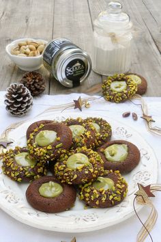 chocolate cookies with pistachios and nuts on a white plate next to a jar of nut butter