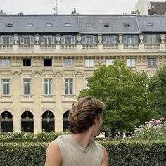 a woman is sitting on a bench in front of a large building with many windows