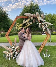 a bride and groom standing in front of an arch decorated with flowers, feathers and candles