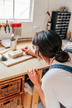 a woman sitting at a table working on some type of crafting project in her workshop