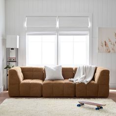 a brown couch sitting on top of a white rug in a living room next to a window