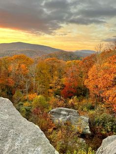 the sun is setting over some rocks and trees with fall foliage in the foreground