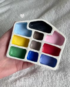 a hand holding a small white tray with different colored paints in it's palm