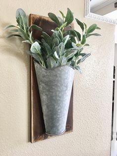 a metal vase filled with green plants on top of a wooden wall mounted planter