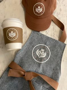 two coffee cups are sitting next to an apron and hat on a marble counter top