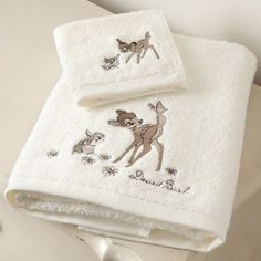 two white towels with embroidered deers on them sitting next to each other in a bathroom