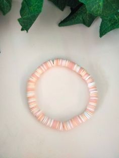 a pink beaded bracelet sitting on top of a white table next to green leaves