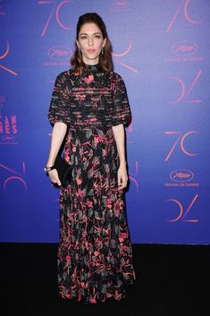 a woman standing in front of a blue wall wearing a black and pink floral dress