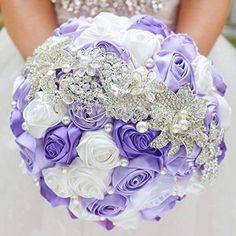 the bride's bouquet is made up of purple and white roses, brooches, and pearls