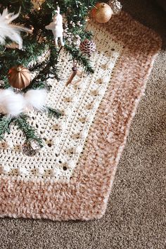 a crocheted christmas tree skirt is on the floor next to a decorated christmas tree