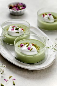 three small desserts on a white plate with flowers in the bowl next to them