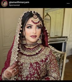 a woman wearing a red and gold bridal outfit with jewelry on her head, in front of a mirror