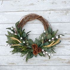 a wreath with greenery and pine cones on a white wooden background, hanging from the wall