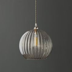 a clear glass ball hanging from a gold chain on a gray wall with a light bulb in the middle