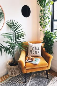 a yellow chair with a pillow and some plants in it next to a wall mounted clock