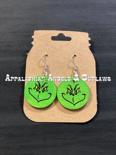 the grin face earrings are green with yellow eyes and black ears, on top of a cardboard