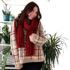 a woman standing in front of a potted plant wearing a red scarf and boots