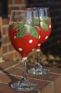 two wine glasses sitting on top of a brick wall next to each other, decorated with holly and white polka dots