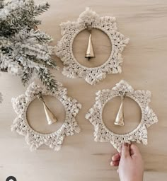 three ornaments are hanging on the wall next to a christmas tree and a person's hand