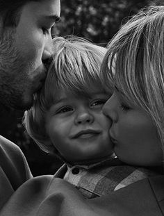 a black and white photo of a man kissing a woman's face with two small children