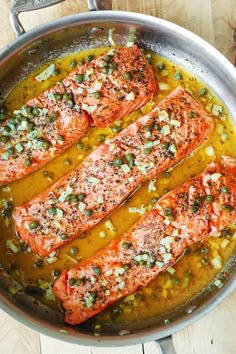 three salmons are cooking in a pan on the stove top, with green onions and seasonings