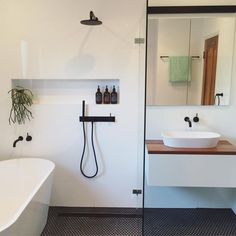 a white bathtub sitting next to a sink under a bathroom mirror with a black faucet