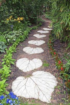 a garden path with white stepping stones and blue flowers on either side, surrounded by greenery