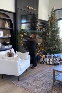 a woman is decorating a christmas tree in her living room with white furniture and black walls