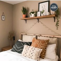 a bed topped with lots of pillows next to a shelf filled with potted plants