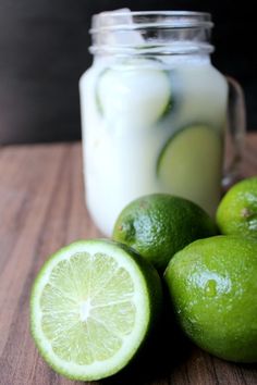 some limes are sitting on a table next to a mason jar with liquid in it