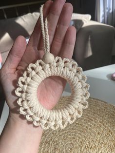 a hand is holding a crocheted ring ornament in front of a couch