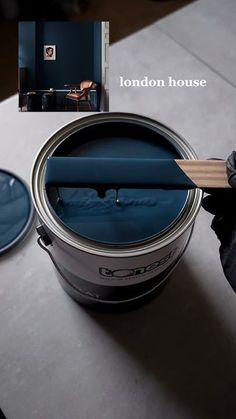 a person is holding a paintbrush over a blue bucket with the lid open and it's inside